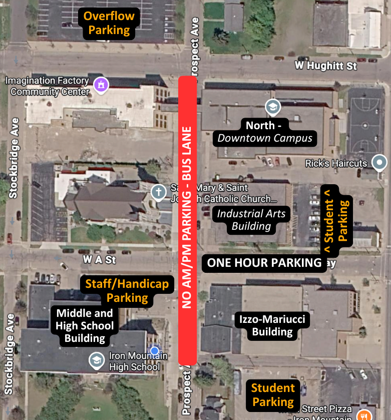 An updated aerial map of the Iron Mountain High School downtown campus detailing surrounding buildings, designated parking areas, and bus route restrictions:  Bus Lane Restriction: A prominent red banner along Prospect Ave marks "NO AM/PM PARKING - BUS LANE" running north-south through the center of the campus map.  Parking Locations:  Staff/Handicap Parking: Located in the lot directly north of the Middle and High School Building, along the south side of W A St.  Student Parking: Main lot located south of the Izzo-Mariucci Building, plus an eastern lot along Way.  One Hour Parking: Located along Way, directly south of the Industrial Arts Building.  Overflow Parking: Located in the lot north of W Hughitt St.  Key Buildings: Middle and High School Building (southwest), Izzo-Mariucci Building (southeast), Industrial Arts Building and North - Downtown Campus (northeast), Saint Mary & Saint Joseph Catholic Church (west of Prospect Ave), and Imagination Factory Community Center (northwest).